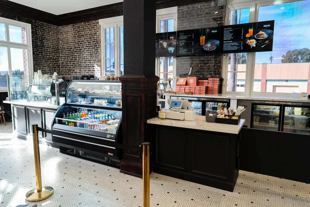 Order counter inside Gud2Go in Pomona — pastry case, digital menu boards, and exposed brick walls.