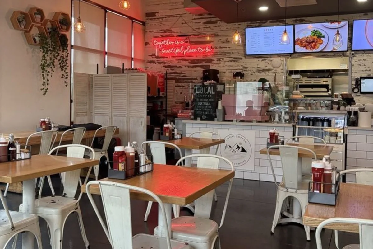 Dining room inside Take Ur Seat Chino Hills — wood tables, white metal chairs, and a neon sign reading 'Together is a beautiful place to be'.