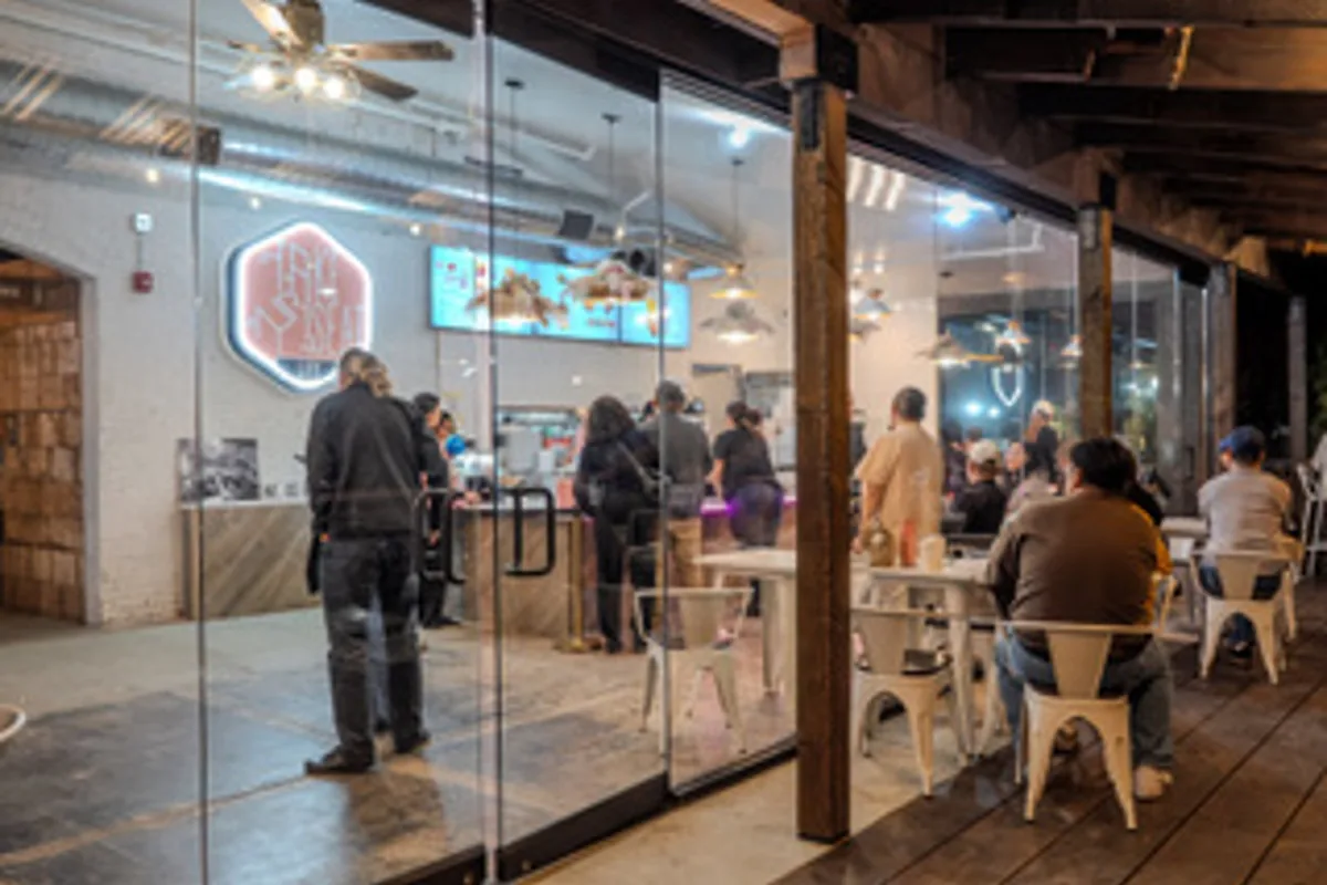 The Take Ur Seat Lite counter inside Redlands Public Market, with guests ordering under the hexagon logo sign.