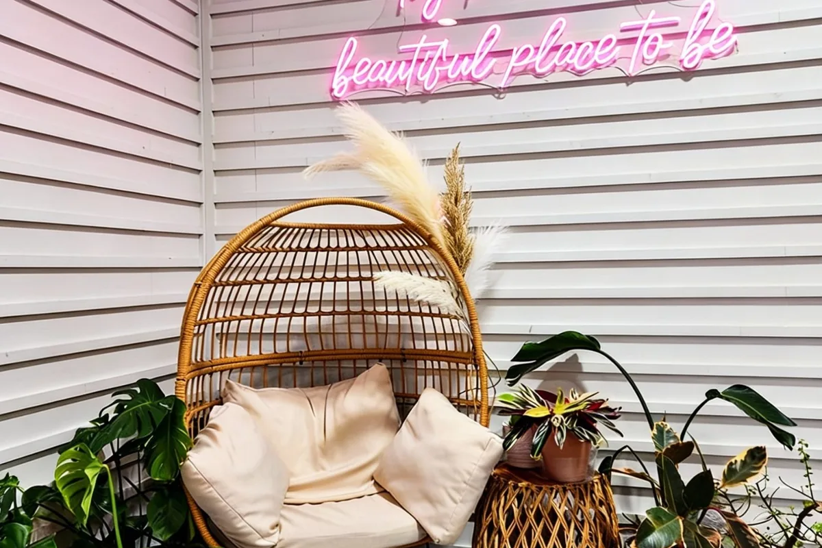 Interior corner at Take Ur Seat Too Ontario — a hanging rattan chair, tropical plants, and a pink neon script sign.