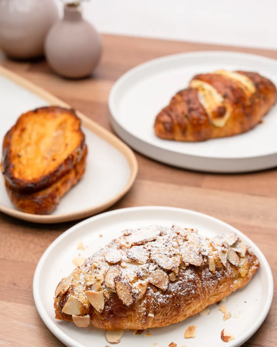 Almond croissant topped with sliced almonds, with a garlic cream cheese croissant and a twice-baked croissant behind it